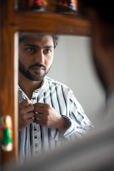 Reflection on a mirror of an young and handsome Indian Bengali brunette man wearing formal shirt before going out in the morning. Indian lifestyle