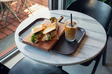 Chicken sandwich with iced coffee on the table in cafe