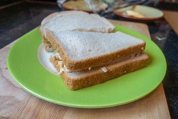 Homemade sandwich with white bread on a green plate on a wooden chopping board for lunch