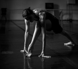 Fototapeta na wymiar Contemporary Dancer rehearsals in ballet studio stretching her body black and white hard contrast studio shot