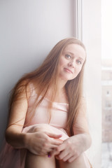 Young attractive woman with beautiful long hair sitting near window looking at camera smiling