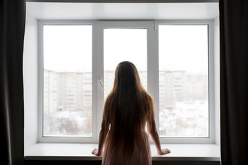 Rear view of woman silhouette standing near window looking out