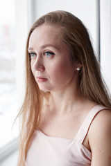 Close-up portrait of real candid beautiful woman with gray eyes and long hair, looking out the window