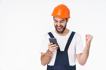 Positive young man builder in helmet using mobile phone.