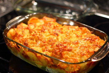 Baked potatoes with cheese in a glass bowl, standing on a black background.