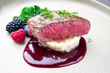 Fried dry aged venison tenderloin fillet medallion steak natural with mashed potatoes and raspberry sauce as closeup on a modern design plate