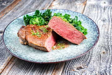 Traditional barbecue dry aged sliced wagyu sirloin beef steak with kalette and herbs as closeup on modern design plate on a wooden board