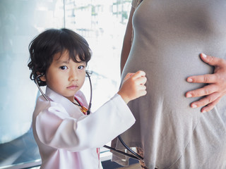Kid girl with stethoscope checking. to pregnant mother's belly