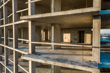 Interior of a concrete residential apartment building room with unfinished bare walls and support pillars for future walls under construction.