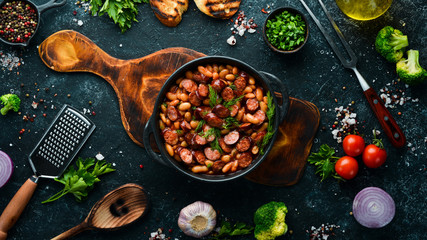 Beans with sausages in tomato sauce on a black plate.  Top view. Free space for your text.