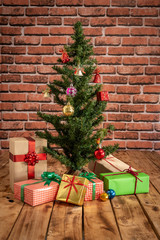 Decorated Christmas tree with gifts box on wooden table with brick wall background