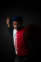 Fashion portrait of an young Indian Bengali brunette man in casual tee shirt and head band playing with basket ball in black copy space background. Indian lifestyle and fashion photography.