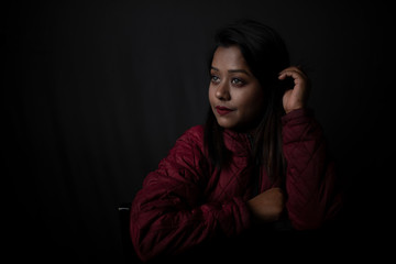 Fashion portrait of an young Indian Bengali brunette woman with maroon winter jacket in black copy space background. Indian lifestyle and fashion photography.