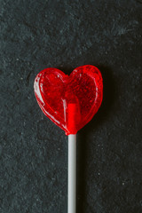 Heart shaped red lollipop on black slate background. Heart shaped red candy for design. Love and Valentines day concept.  