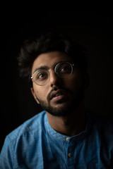 Fashion portrait of young and handsome Indian Bengali brunette man with traditional cotton wear and glasses in black copy space background. Indian lifestyle and fashion photography.