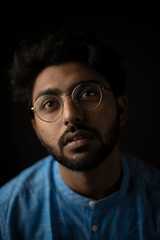 Obraz premium Fashion portrait of young and handsome Indian Bengali brunette man with traditional cotton wear and glasses in black copy space background. Indian lifestyle and fashion photography.