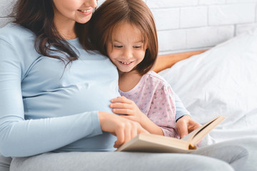 Close up of excited girl reading book with expecting mother