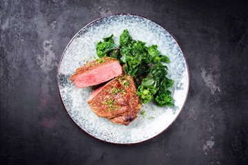 Traditional barbecue dry aged sliced wagyu sirloin beef steak with kalette and herbs as top view on modern design plate on a rustic board