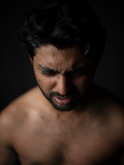 Portrait of young and handsome Indian Bengali brunette man in bare body crying loudly in black copy space background. Indian lifestyle and fashion photography