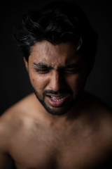 Fototapeta premium Portrait of young and handsome Indian Bengali brunette man in bare body crying loudly in black copy space background. Indian lifestyle and fashion photography
