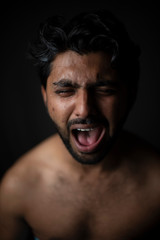 Portrait of young and handsome Indian Bengali brunette man in bare body crying loudly in black copy space background. Indian lifestyle and fashion photography