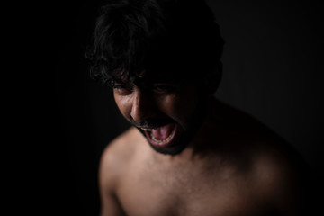 Portrait of young and handsome Indian Bengali brunette man in bare body crying loudly in black copy space background. Indian lifestyle and fashion photography