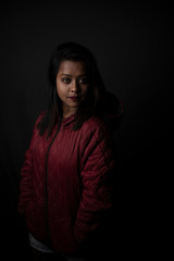 Fashion portrait of an young Indian Bengali brunette woman with maroon winter jacket in black copy space background. Indian lifestyle and fashion photography.