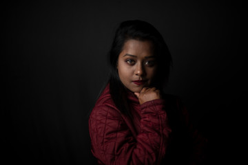 Fashion portrait of an young Indian Bengali brunette woman with maroon winter jacket in black copy space background. Indian lifestyle and fashion photography.