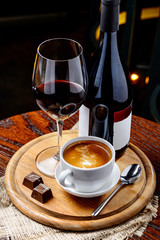 A bottle of red wine with cup of coffee and chocolate on wooden table