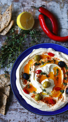 Selective focus. Hummus on a blue plate with olives, chili and thyme.