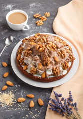 Homemade cake with milk cream, cocoa, almond, hazelnut on a black concrete  background with orange textile and a cup of coffee. Side view.