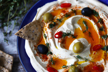 Selective focus. Hummus on a blue plate with olives, chili and thyme.