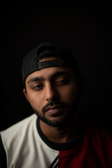 Fashion portrait of young and handsome Indian Bengali brunette man with casual tee shirt showing facial expression in black copy space background. Indian lifestyle and fashion photography