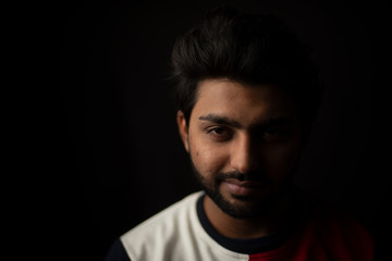 Obraz premium Fashion portrait of young and handsome Indian Bengali brunette man with casual tee shirt showing facial expression in black copy space background. Indian lifestyle and fashion photography