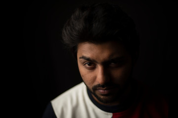 Fashion portrait of young and handsome Indian Bengali brunette man with casual tee shirt showing facial expression in black copy space background. Indian lifestyle and fashion photography