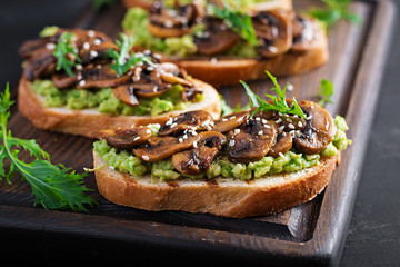 Bruschetta. Sandwich with avocado, fried mushrooms, sesame on a wooden board. Vegetarian food. Vegan menu.