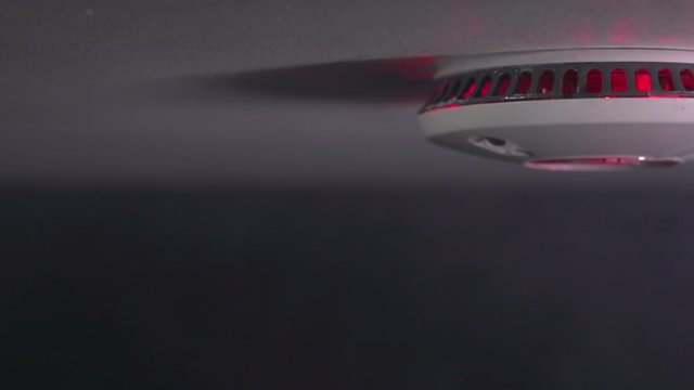 Smoke alarm detector with smoke rising - The light is flashing as there is a fire. Tracking shot