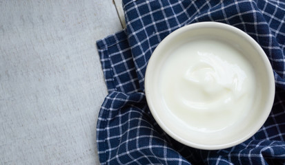 Natural white yogurt on white cup on napkins white wooden table.Top view.