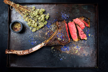 Barbecue dry aged wagyu tomahawk steak with herbs as top view on black rustic board