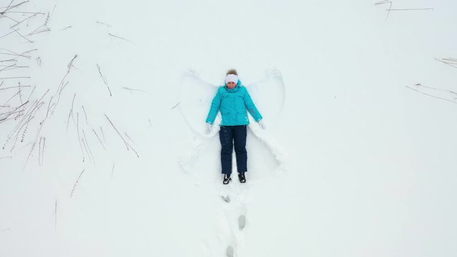 A girl makes a figure of a snow angel in a clearing in the forest. Aerial photography of a girl lying in the snow.