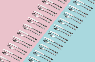 Knife and fork flat lay pattern on pastel pink and blue background. Many metallic forks, and knives top view concept Background for menu Restaurant backdrop. Creative top view pattern Copy free space.