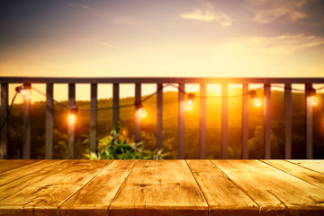 Wooden board of free space for your decoration. Blurred background of balcony and ladnscape of Tuscany.Small lights and orange color of sunset time.  - obrazy, fototapety, plakaty