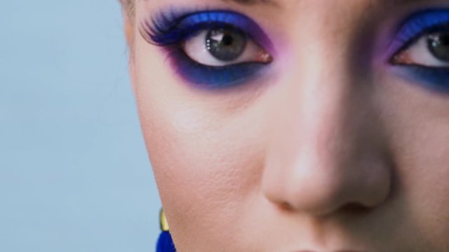 Glamorous bright eye makeup using the trend color classic blue, women's eyes close-up. girl opens her eyes and looks at the camera, Blue shadows and earrings