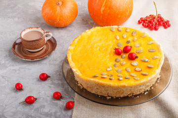 Traditional american sweet pumpkin pie decorated with hawthorn red berries and pumpkin seeds with cup of coffee on a gray concrete background. side view.