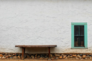 Fototapeta na wymiar Small wooden bench near an adobe wall with a window