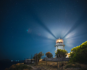 White sea lighthouse in Feodosia, Crimea on the Black Sea with rays of light under the night sky
