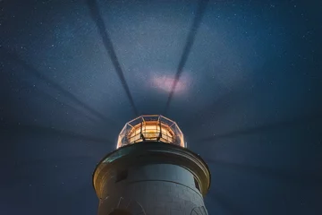 Dekokissen the sea lighthouse shines at night with bright rays of light against the background of the starry sky © Ambartsumian