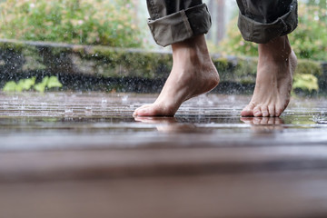 Barefoot female legs walk on the wooden floor of the courtyard, in the pouring summer rain, on a blurred background.