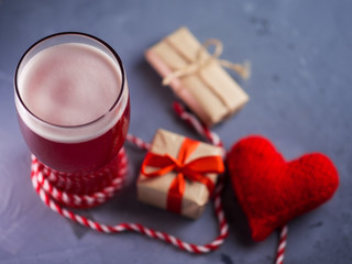 A glass of cold red ale beer on the table with a red heart and gift box