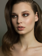 Obraz premium Close-up portrait of the cleanliness face of a beautiful woman with dark black smoky eyes makeup, natural full lips. Sexy model with clean shiny skin, clean face, long curly hair. glamorous image